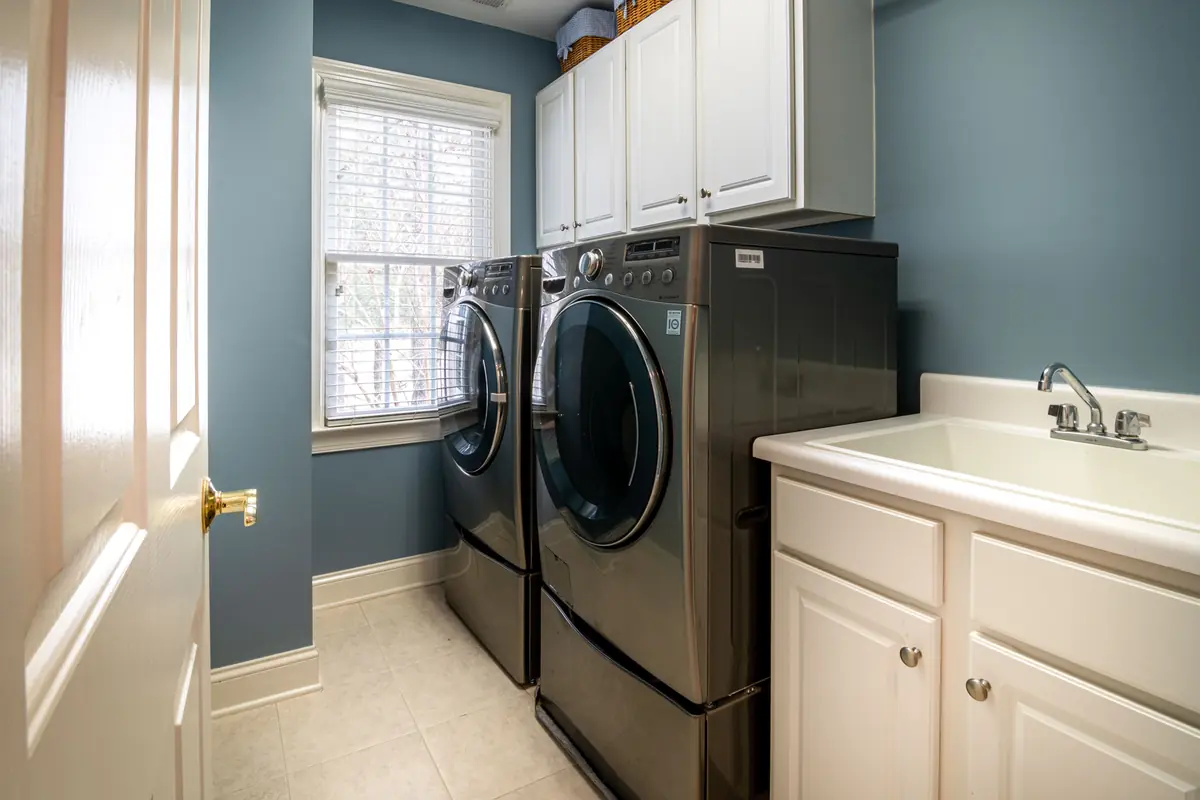 Laundry room with a front-loading washer and dryer on pedestal drawers beside a utility sink and cabinets
