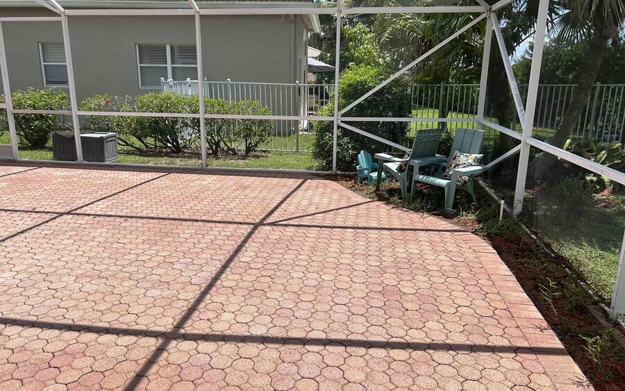 Corner of a screened enclosure after cleaning with clear screen panels and a cleaned paver deck