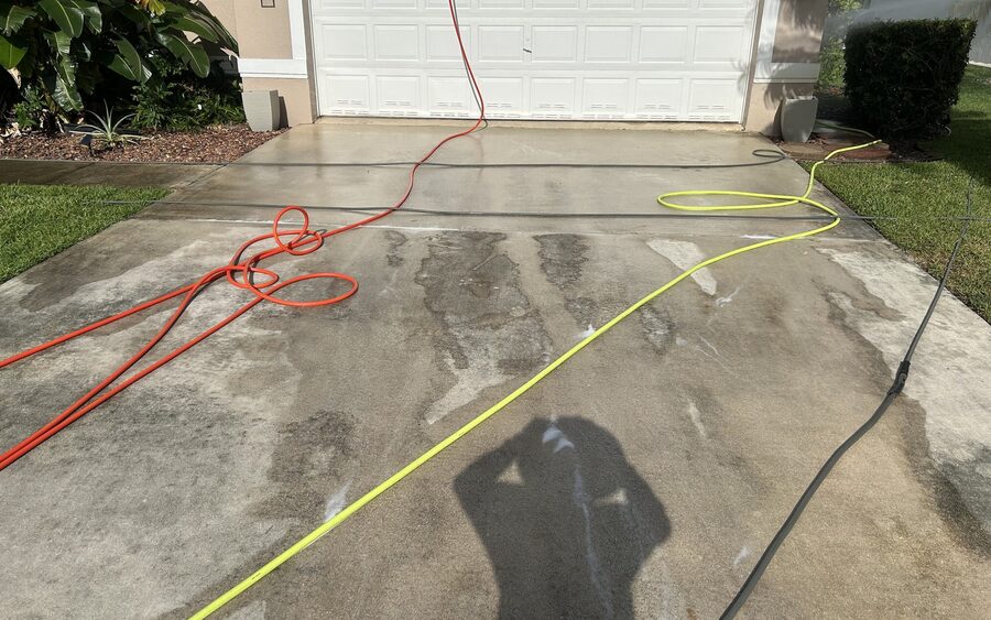 Concrete driveway during pressure washing with hoses run out across the wet surface