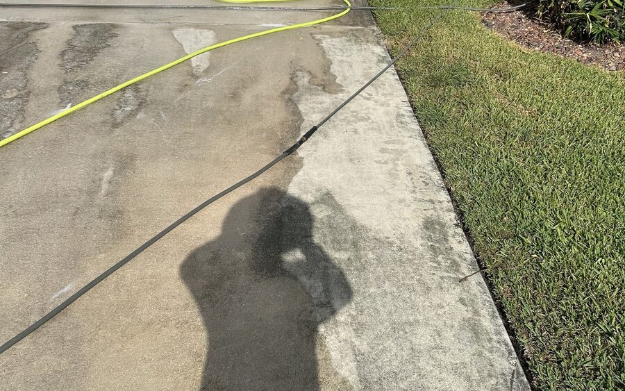 Concrete walkway during pressure washing, both states shown in one image - untreated grey concrete meeting a cleaned lighter section