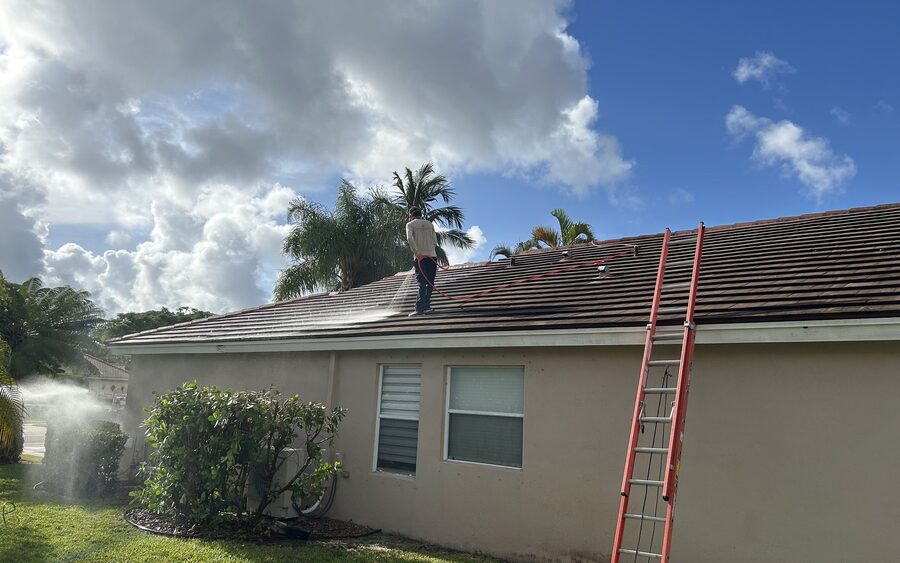 Technician soft washing a tile roof with solution spraying across the tiles
