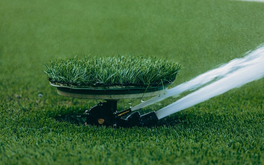 Pop-up lawn sprinkler head spraying a jet of water across cut turf