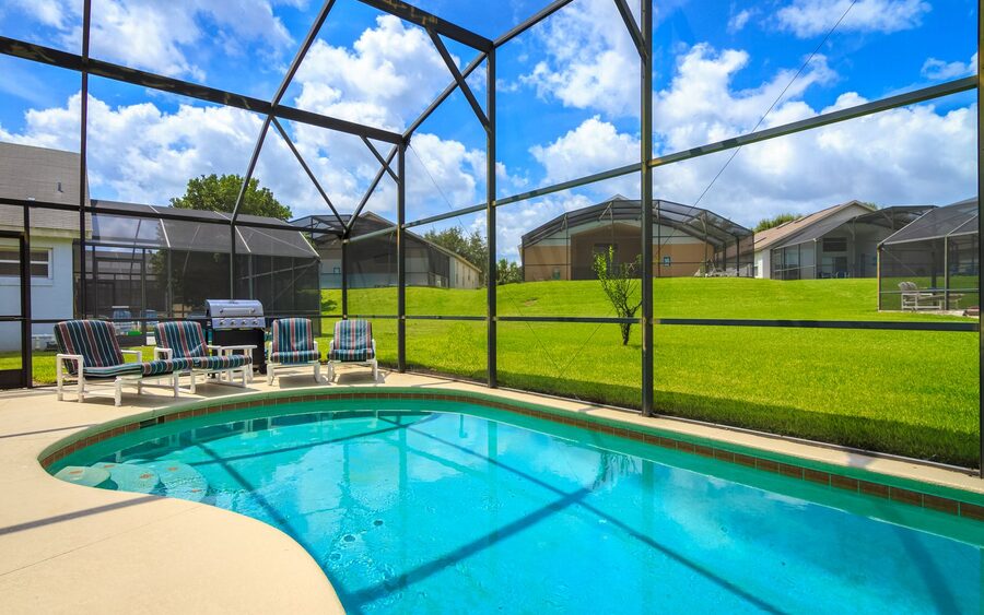 Screened pool enclosure over a swimming pool and lounge chairs under a blue sky