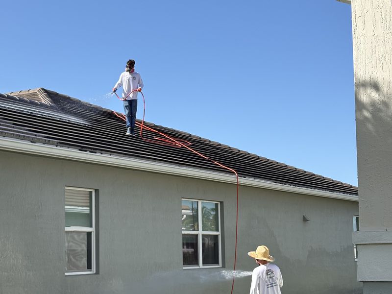 Technician applying low-pressure soft wash to a tile roof to remove algae streaks